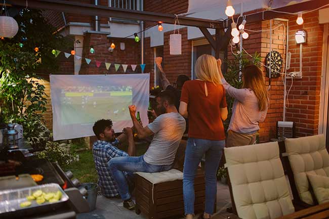 Freunde schauen Fußball auf Leinwand im Garten