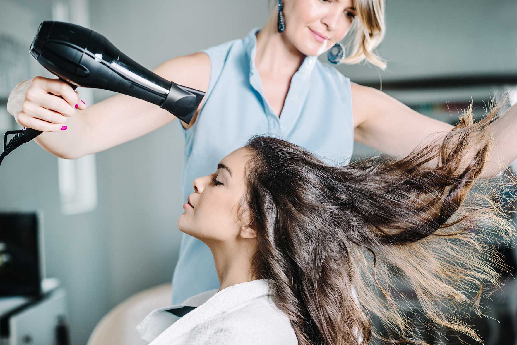 Friseurin trocknet die Haare einer jungen Frau mit dem Haartrockner