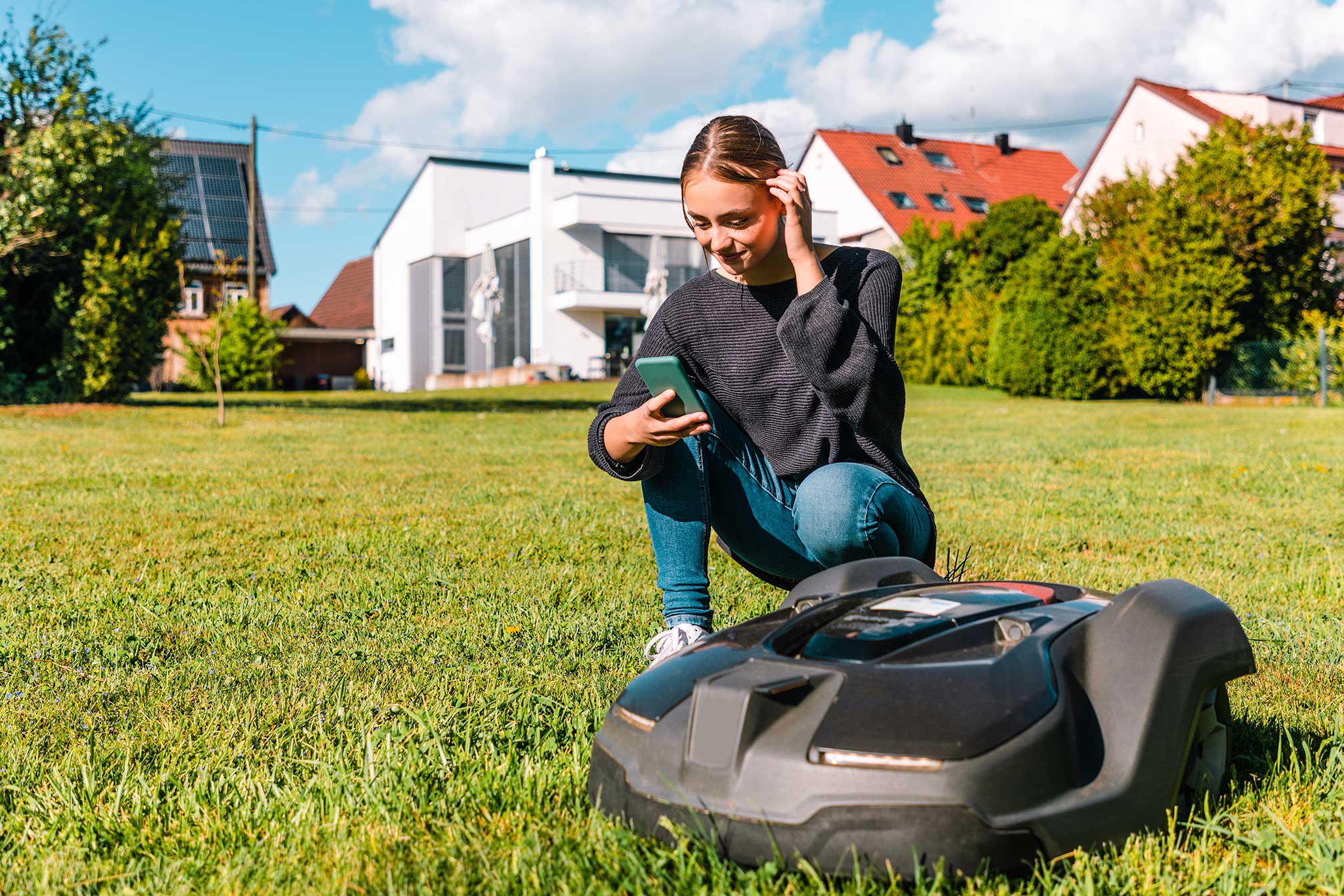 Lächelndes Mädchen neben Rasenmäherroboter
